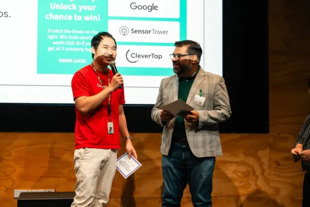 Two men speaking on stage at a Google session, one holding a microphone and the other holding notes