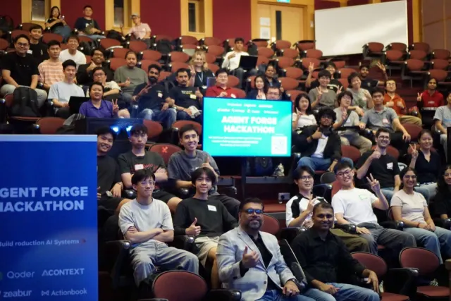 Lecture theatre of attendees raising peace signs beneath Agent Forge Hackathon signage