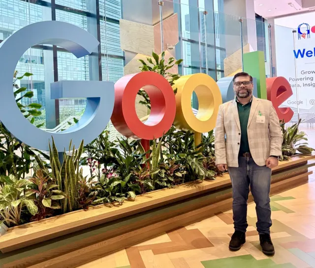 Tanveer Riaz standing beside large multicoloured Google letters in a glass-walled lobby
