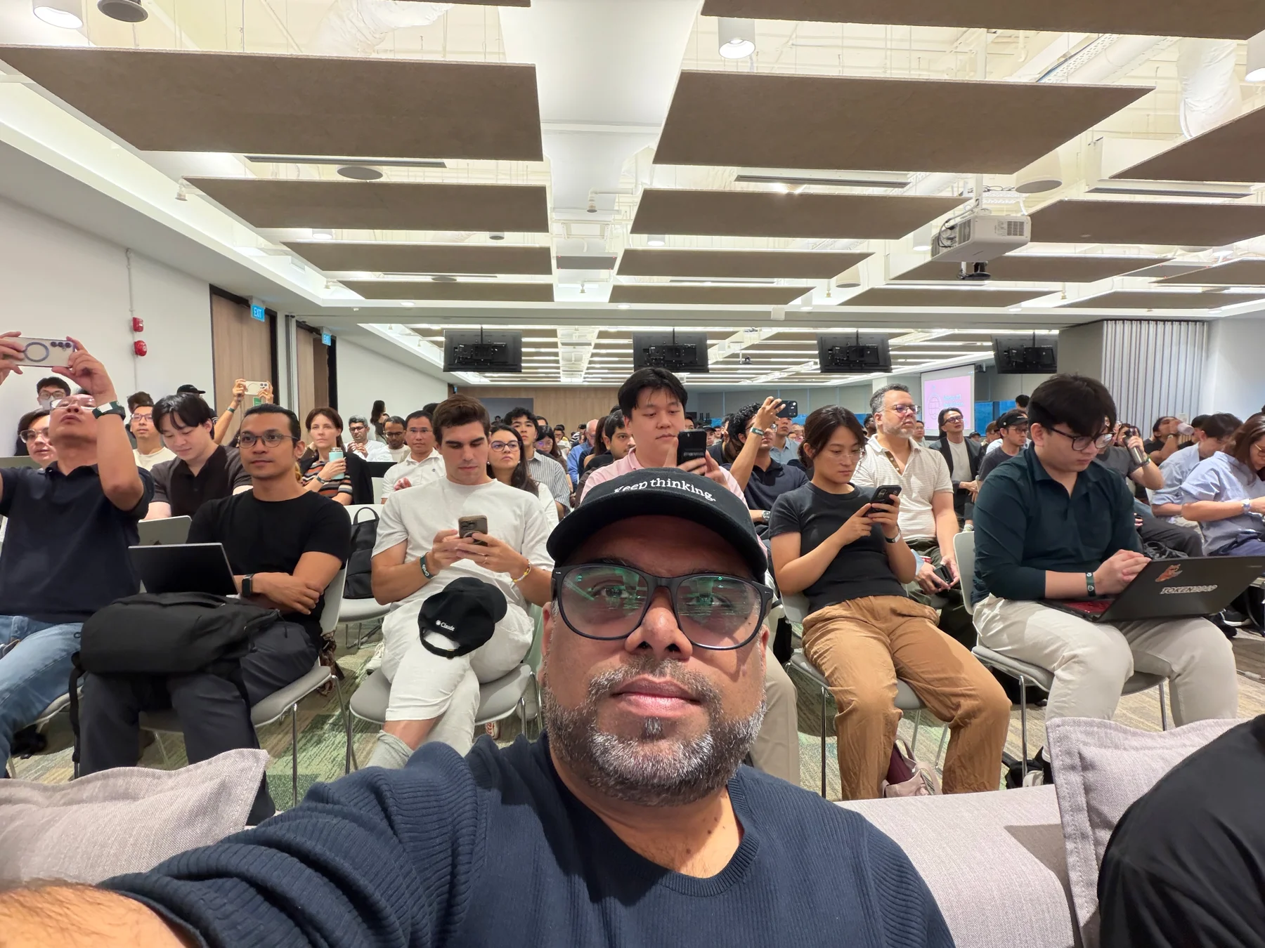 Tanveer Riaz taking a selfie in the audience at the Claude Community event at Grab, with rows of attendees behind him