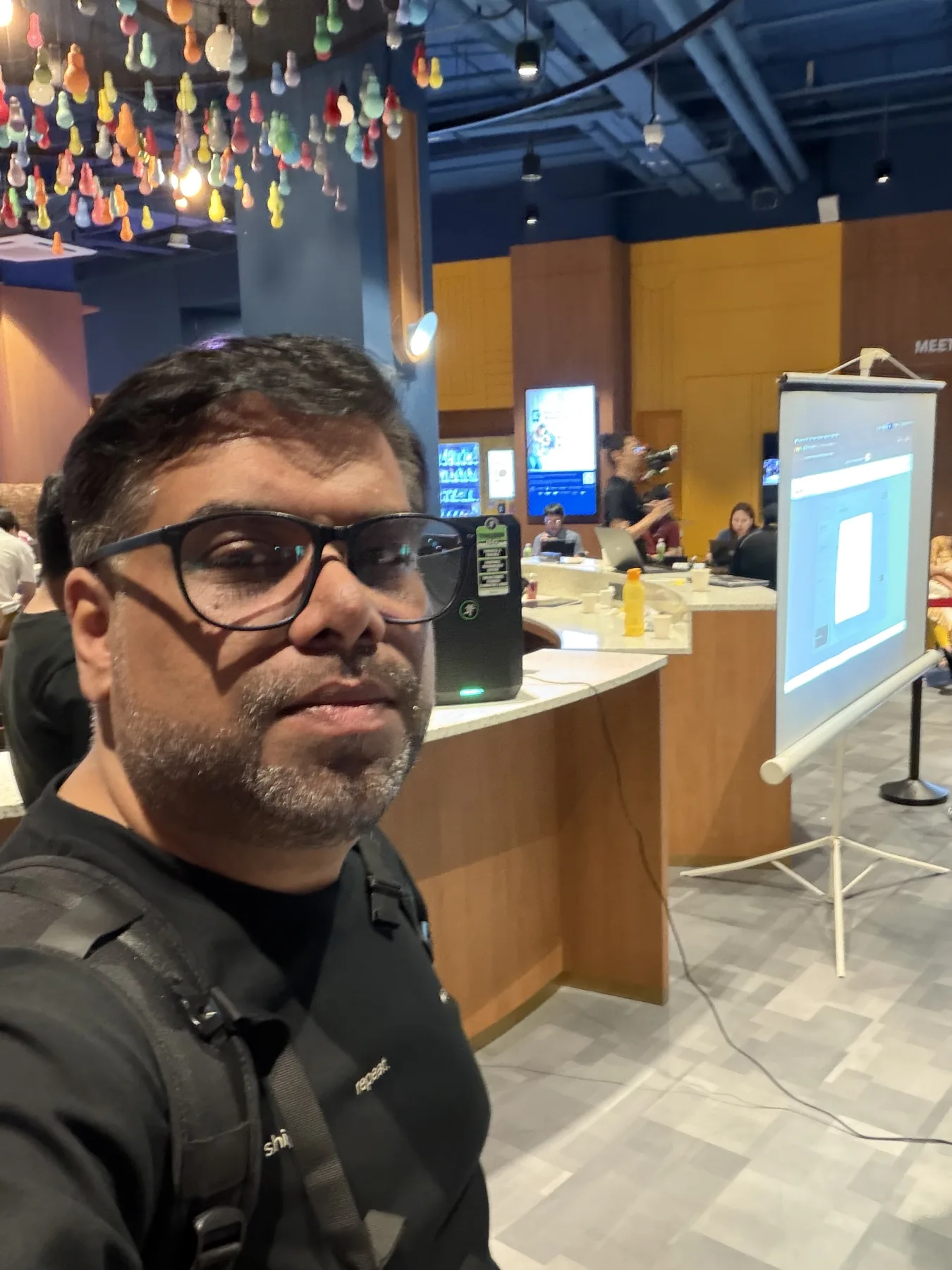 Tanveer Riaz on the ChatGPT Sites Hackathon build floor beside the presentation screen